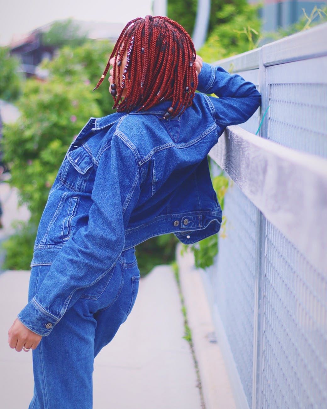 back view photo of woman in denim outfit leaning against metal fence